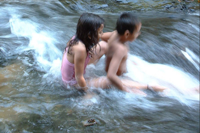 Two young children sliding down natural water slide in a stream