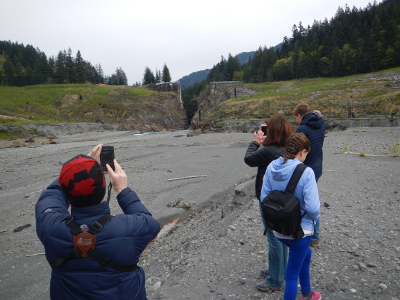 A family takes photos of the towering Glines Canyon Dam Gap from the former Lake Mills