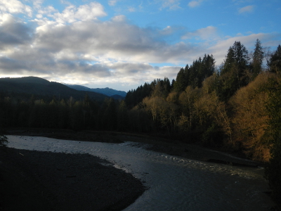 A sunny winter day shows towering conifers, beautiful pink and grey clouds, and blue sky above the Elwha River