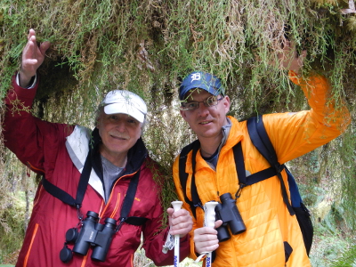 Two smiling multi-generational participants with binoculars part the strands of curtain moss in the Hoh Rainforest