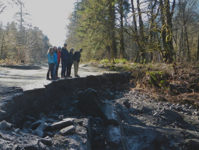 A family stands at the edge of a portion of destroyed roadway in Elwha River Valley