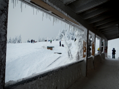 A view looking out towards people playing in the snow from the Hurricane Ridge Visitor Center porch bordered by icicles