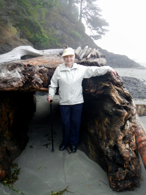 One participants stands smiling next to a huge piece of woody debris on the beach