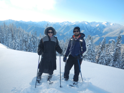 A couple in full winter on an Olympic National Park snowshoe tour pose with the Olympic mountains in the background