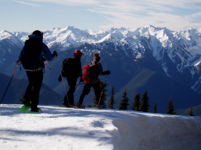 Three people on snowshoes are treated to an amazing view of snow-clad Olympic Mountains at Hurricane Ridge
