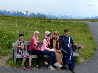 Parents and their three children sit on a wooden bench at Hurricane Ridge with the snowy Olympic Mountains in the distance 