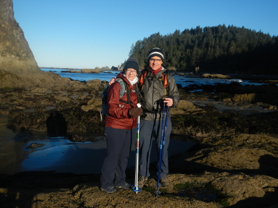A couple stands smiling near Hole in the Wall with the Pacific Coast near shore in the background