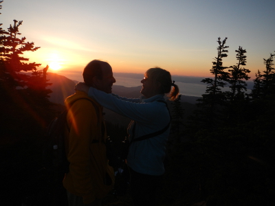 Two embracing hikers look into the eyes of their significant other as the sun sets in the background