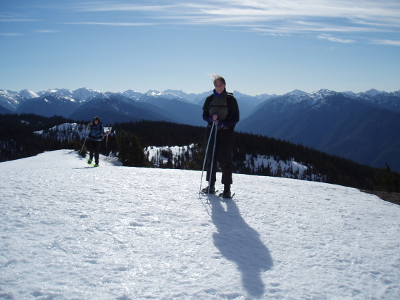 Two people using snowshoes at Hurricane Ridge with snow clad Olympic Mountains in the background