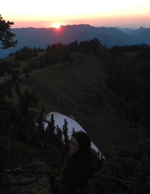 A smiling hiker sits enjoying the sunset over the Strait of Juan de Fuca and some of the Olympic foothills